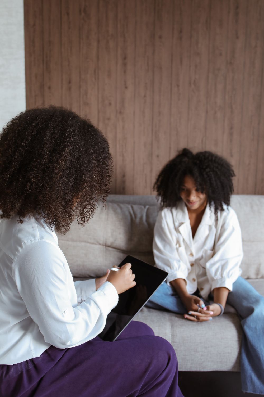 Two women in a reflective conversation on a sofa, one taking notes