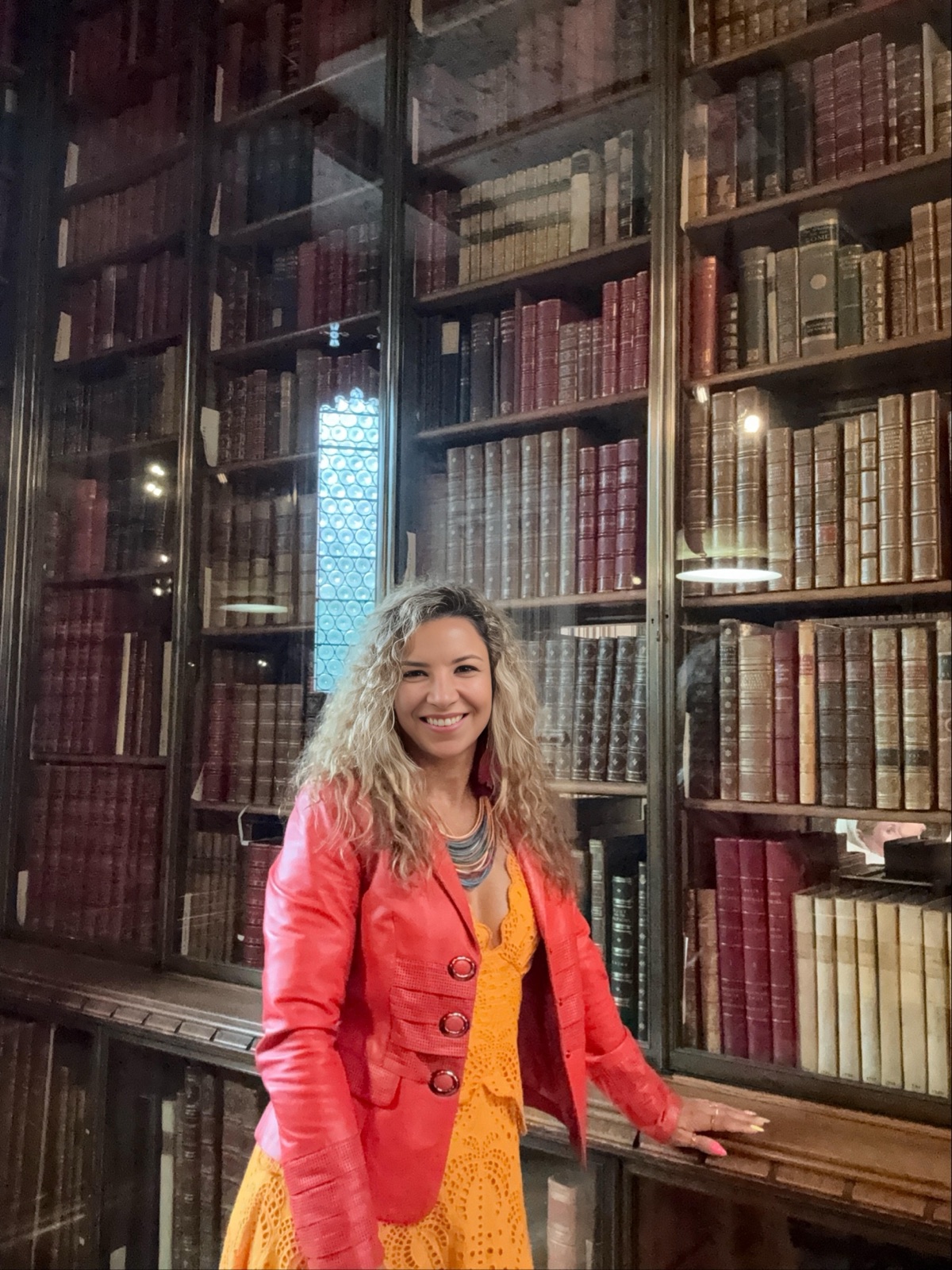 Tati Silva smiling in a historic library, in front of shelves of antique books